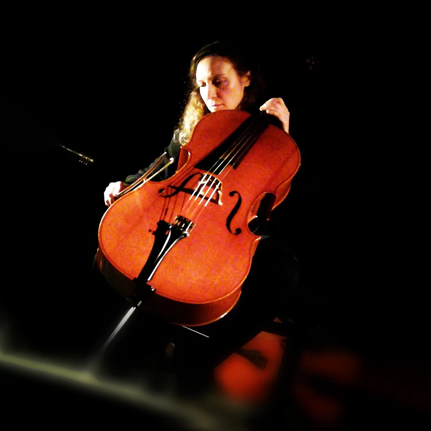 A person is playing a cello in a dimly lit setting, with the instrument prominently visible.