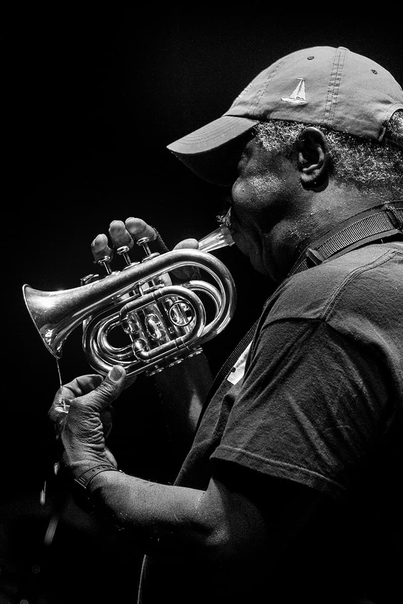 A person wearing a cap plays a cornet, captured in black and white.