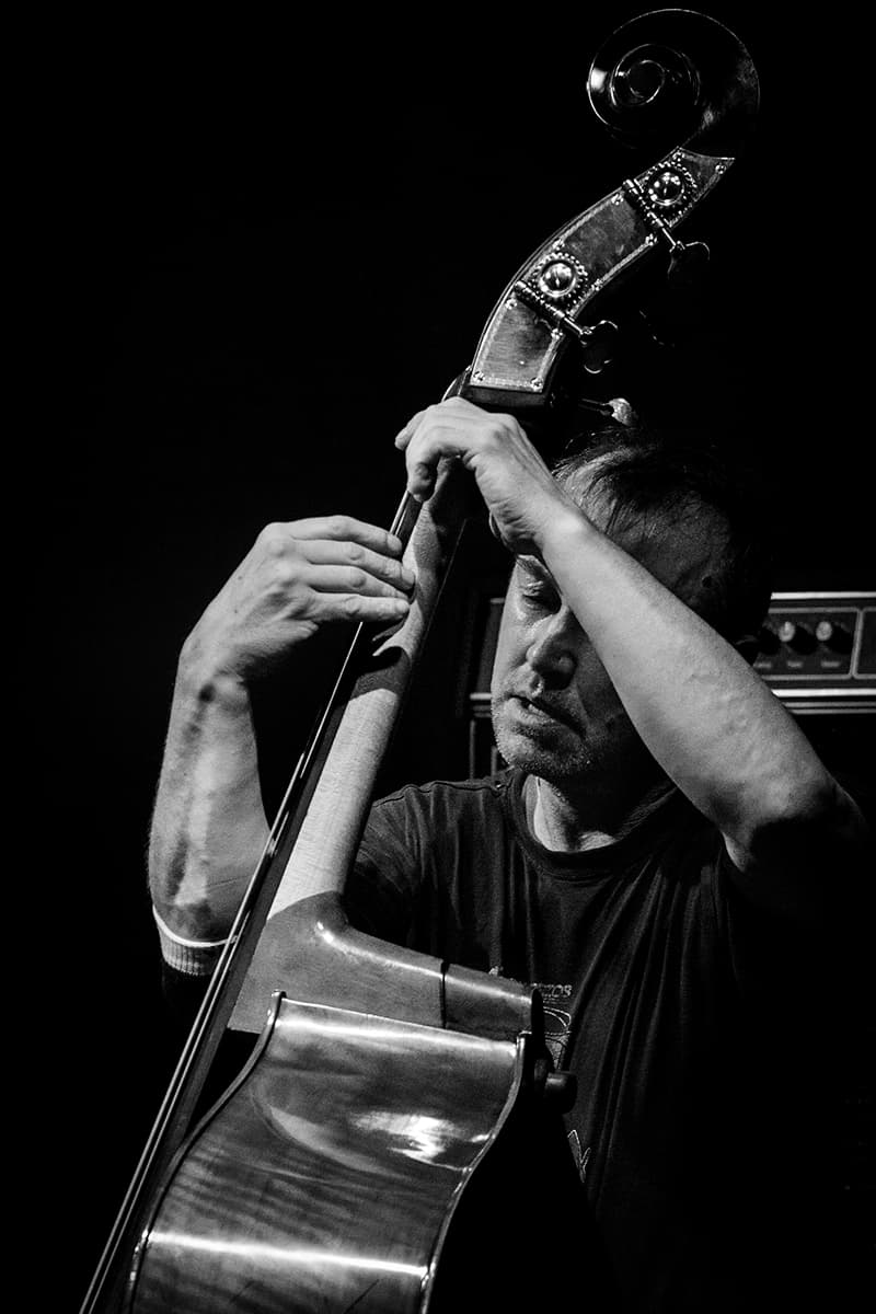 A musician is intensely playing a double bass in a black and white setting.