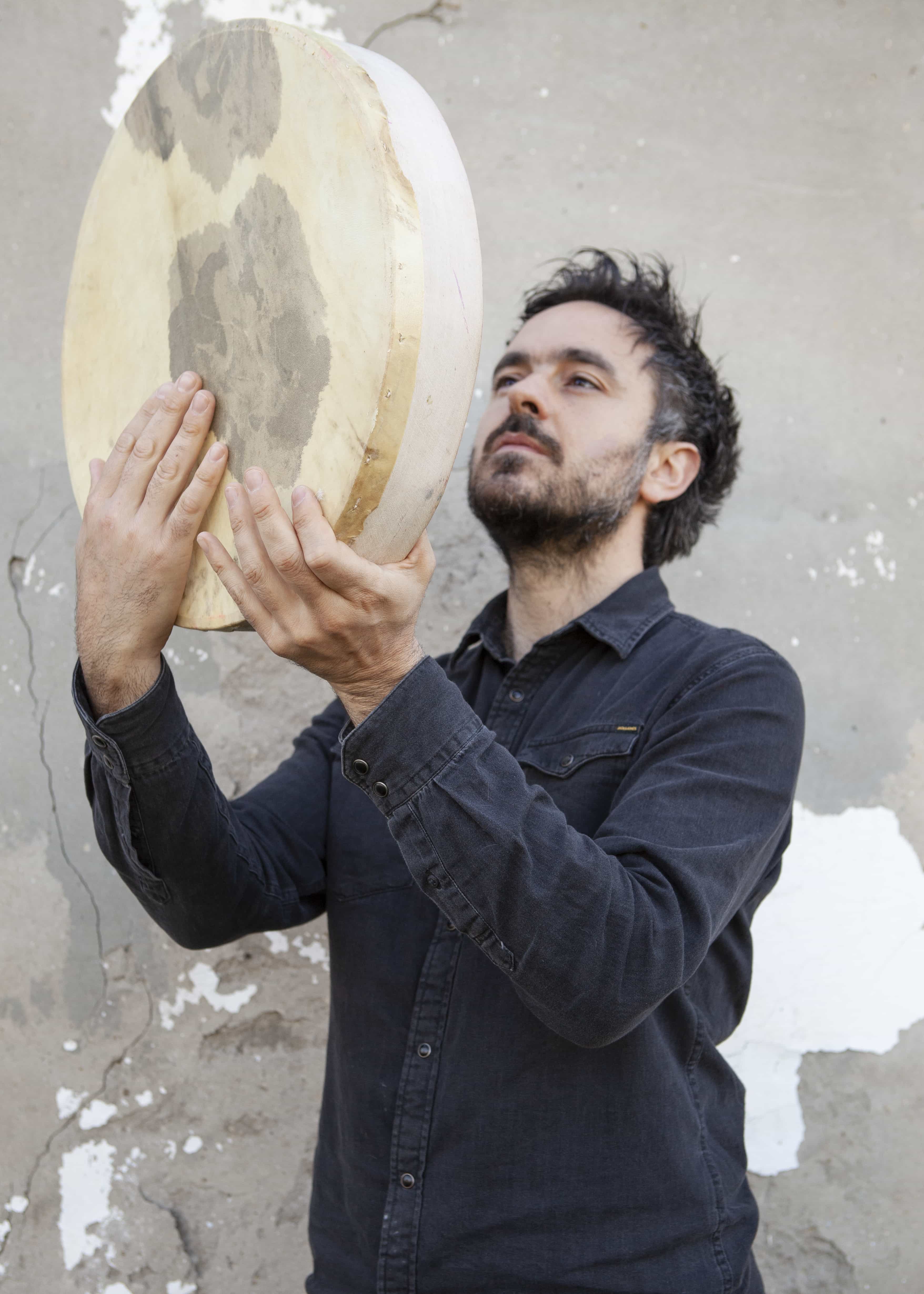 A person in a dark shirt is holding and looking at a large round drum against a textured wall.