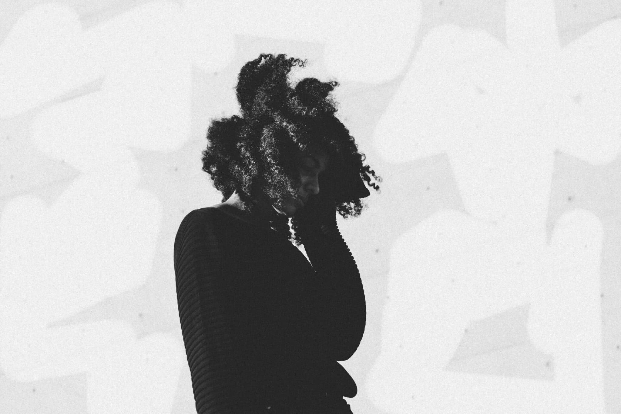 A silhouette of a person with curly hair, wearing a textured sweater, set against a light abstract background.