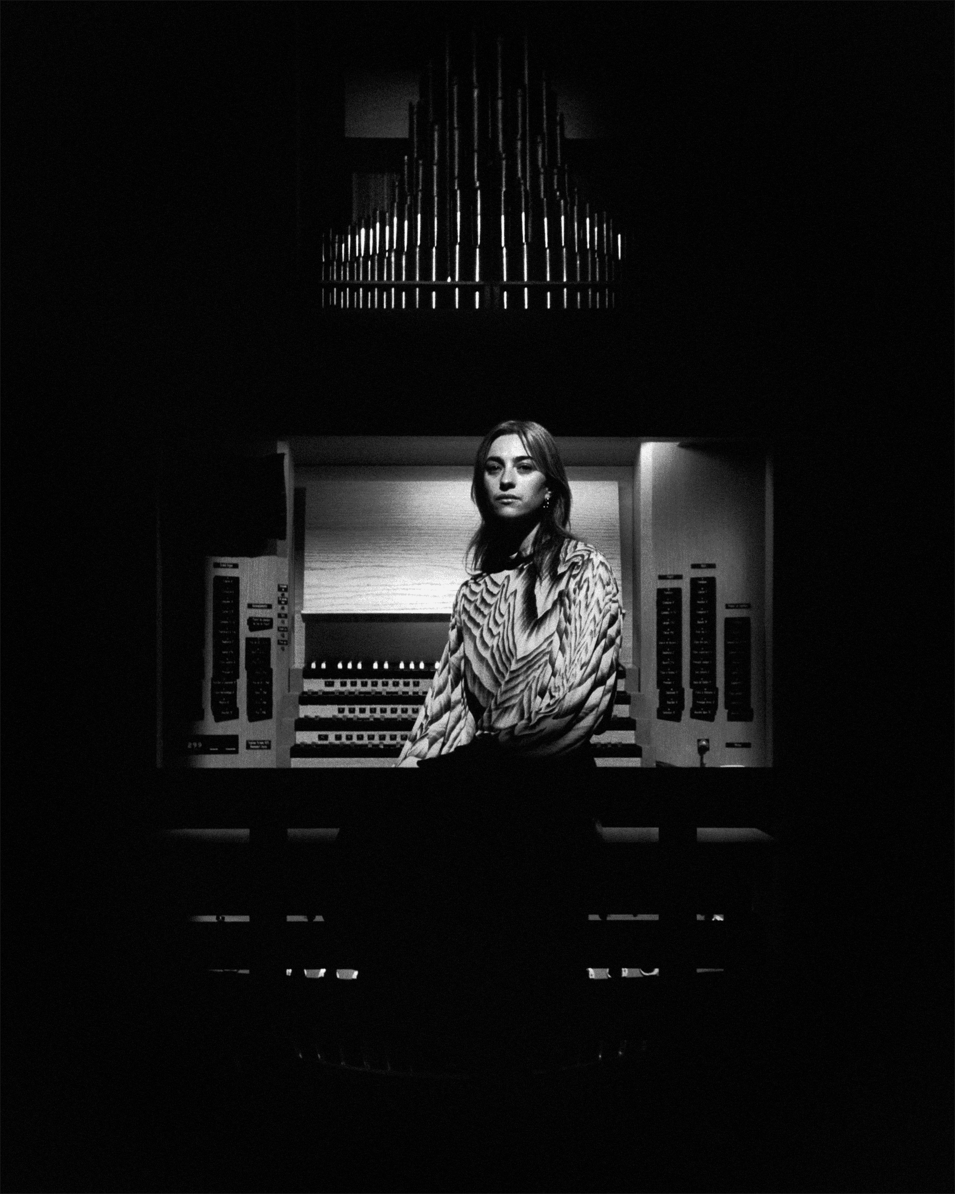 A person stands in front of an organ console, illuminated in a dark setting.