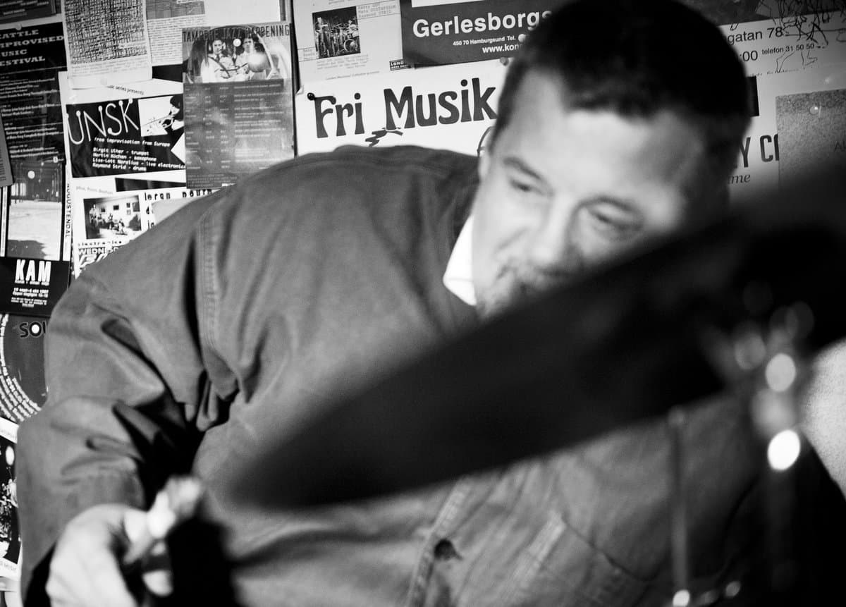 A person is playing drums with a blurred background covered in posters.