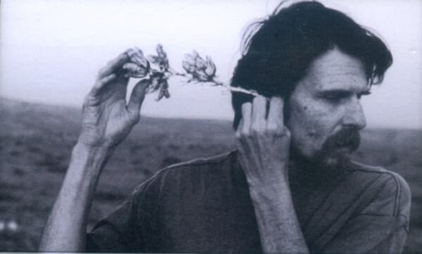 A person is holding a plant to their ear in a desert landscape.