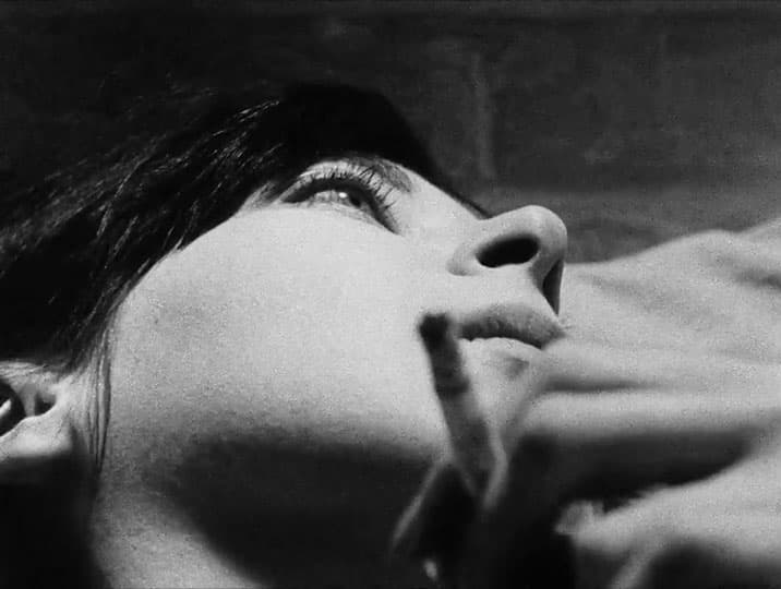 A person is lying down, holding a cigarette, and looking upwards in a black and white close-up shot.