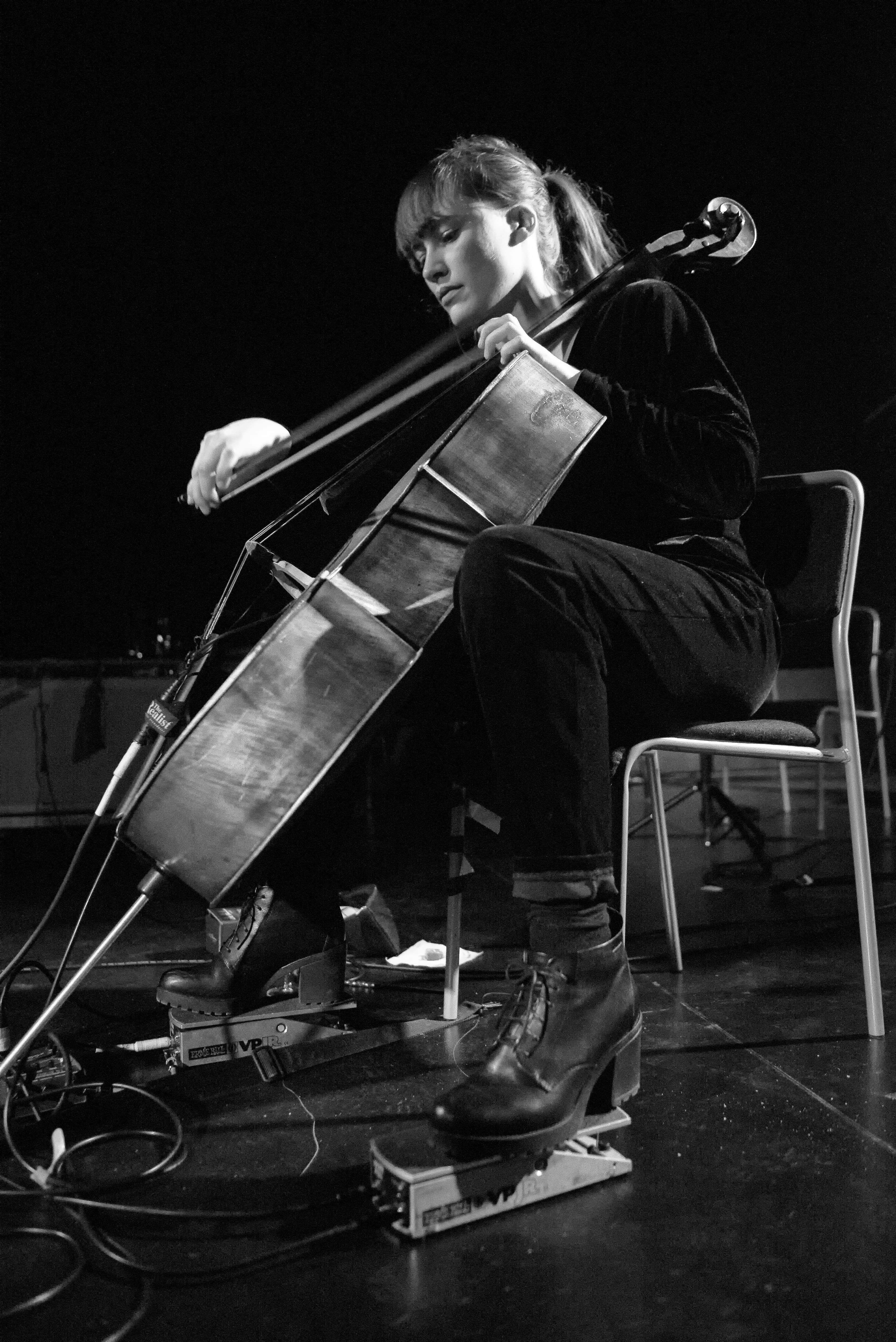 A person is playing a cello while seated, with foot pedals on the floor.