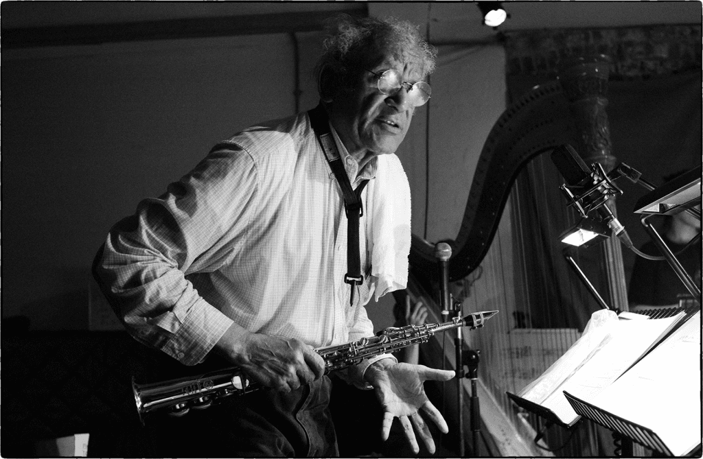 A person is playing a saxophone in a dimly lit room with a music stand and microphone nearby.