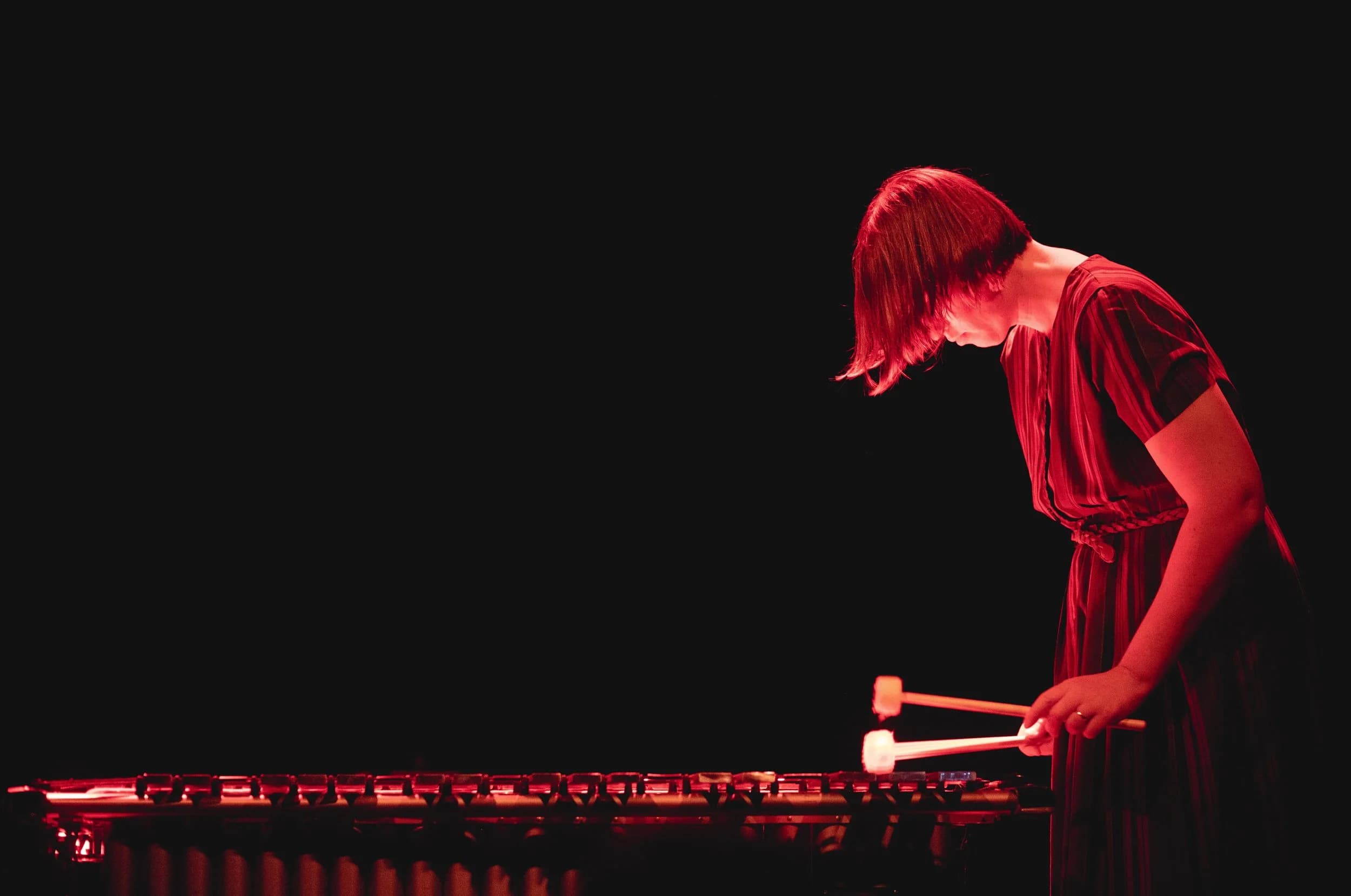 A person is playing a vibraphone on stage, illuminated by red lighting.