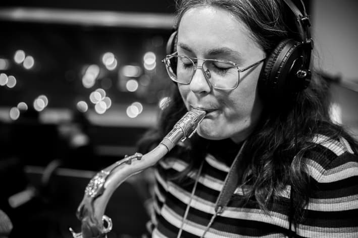 A person wearing headphones and glasses is playing a saxophone.
