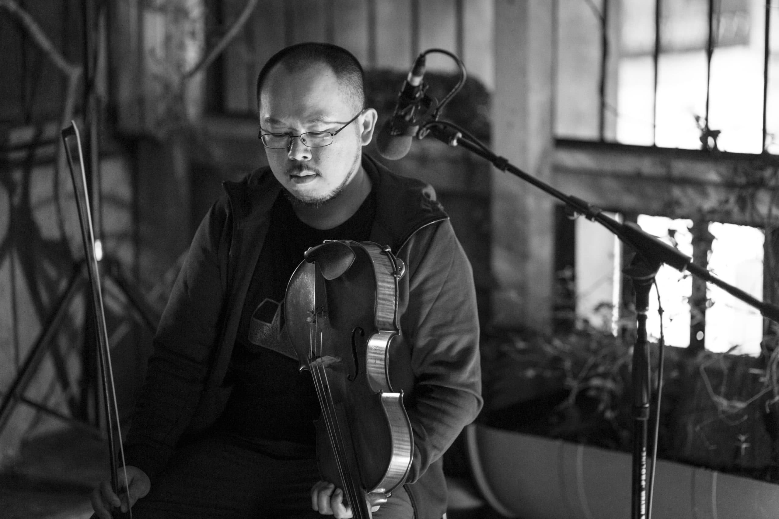 A person is sitting and holding a violin with a microphone nearby.