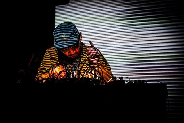 A person wearing a striped shirt and cap is operating electronic equipment, with a striped pattern projected on the background.