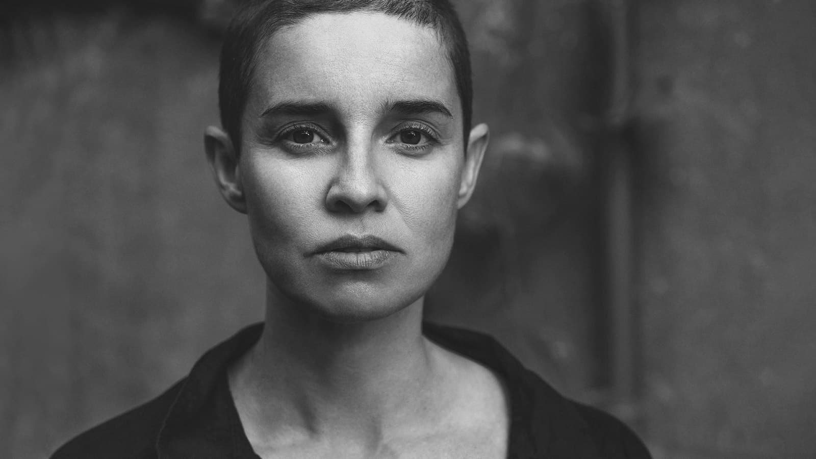 A black-and-white portrait of a person with short hair, looking directly at the camera with a neutral expression.