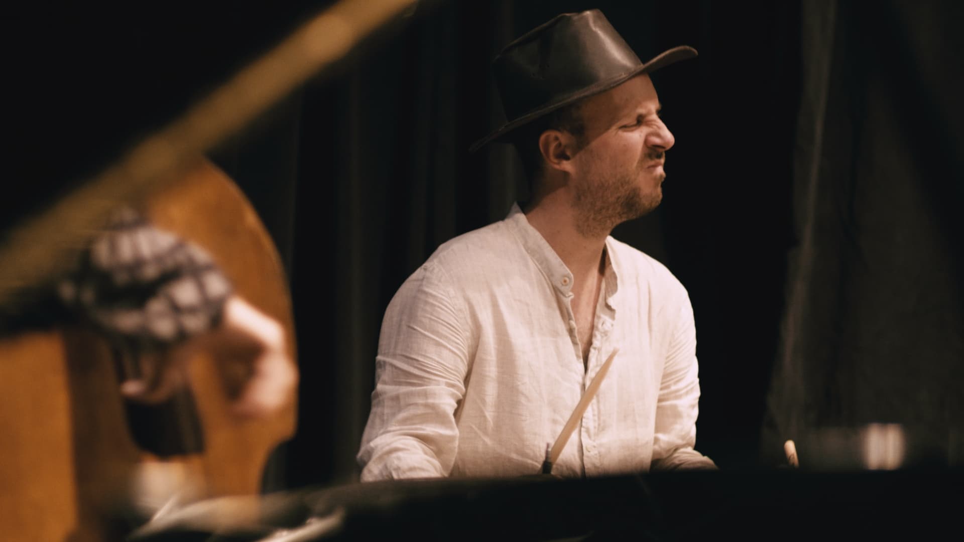 A person in a white shirt and hat is playing drums with a focused expression.