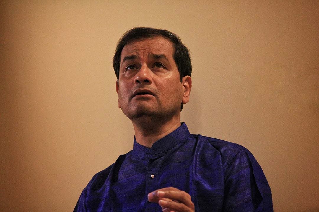 A person in a blue traditional outfit is looking upwards with a contemplative expression.