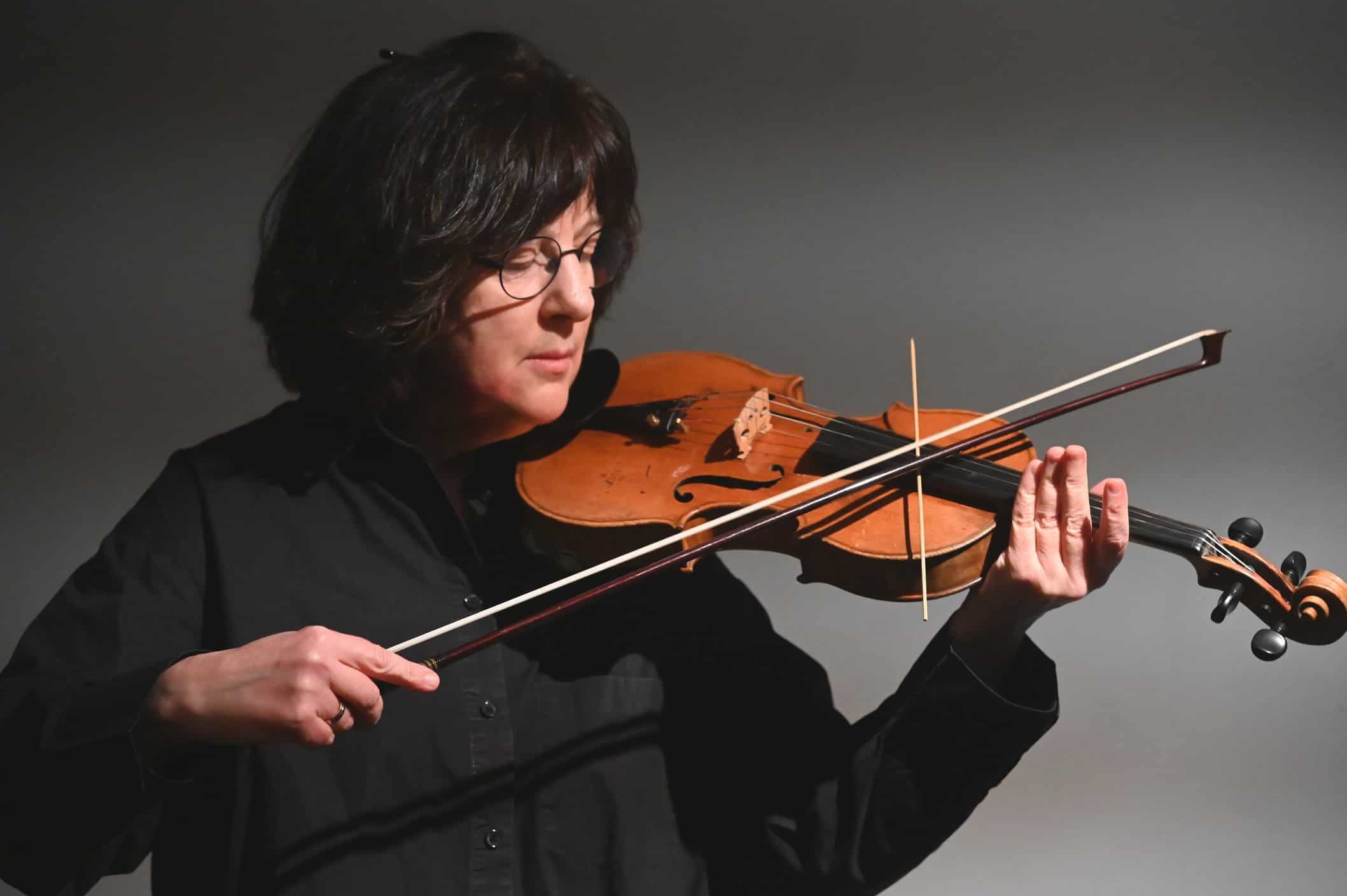 A person with glasses is playing a violin.