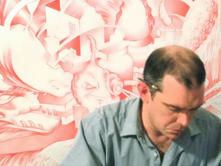 A man with a pencil behind his ear is in front of a surreal, red-toned drawing featuring abstract and fantastical shapes.