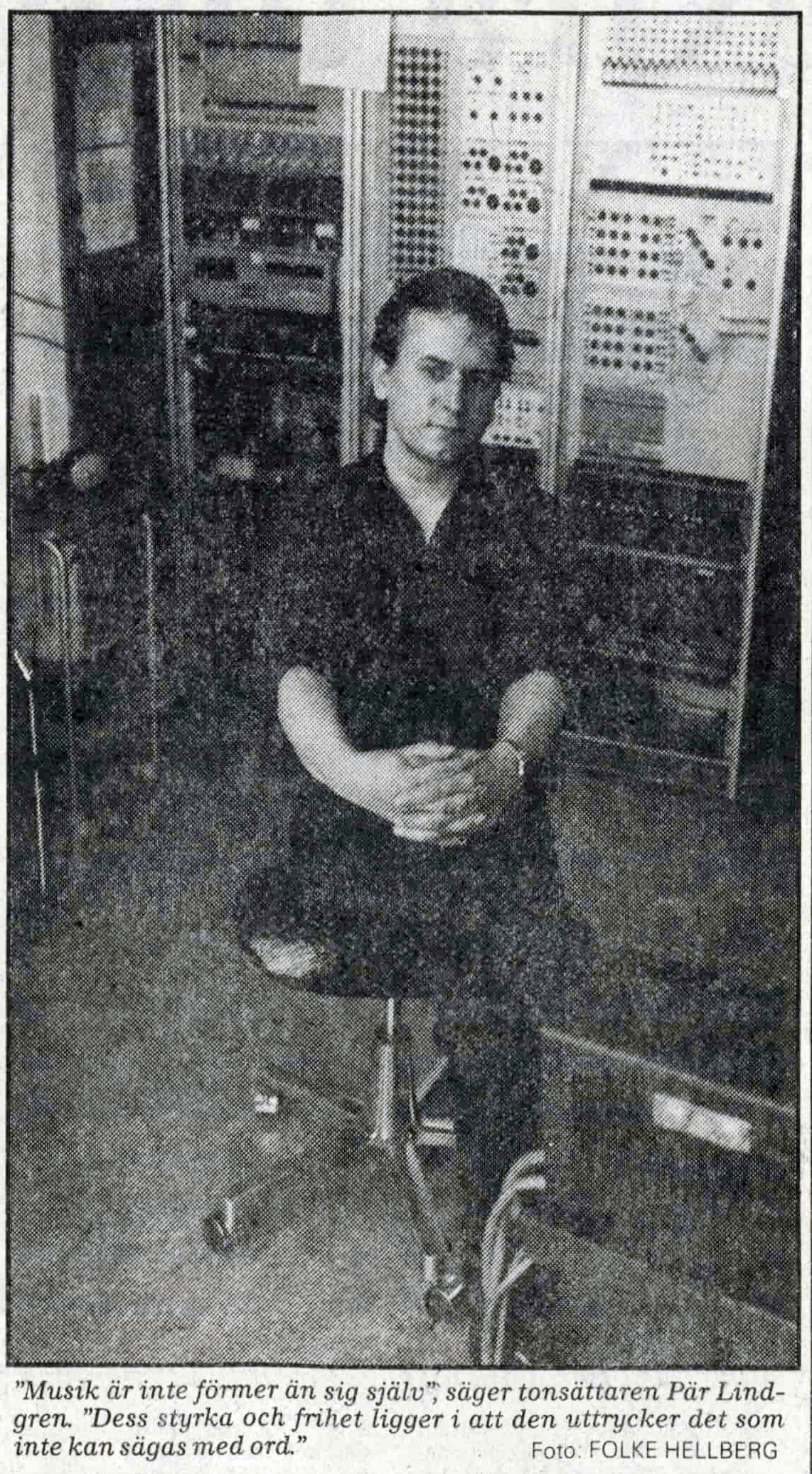 A person is seated in front of a large panel of electronic equipment.