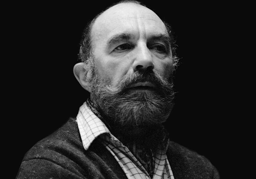 A black-and-white portrait of a bearded man wearing a collared shirt and sweater, with a serious expression.