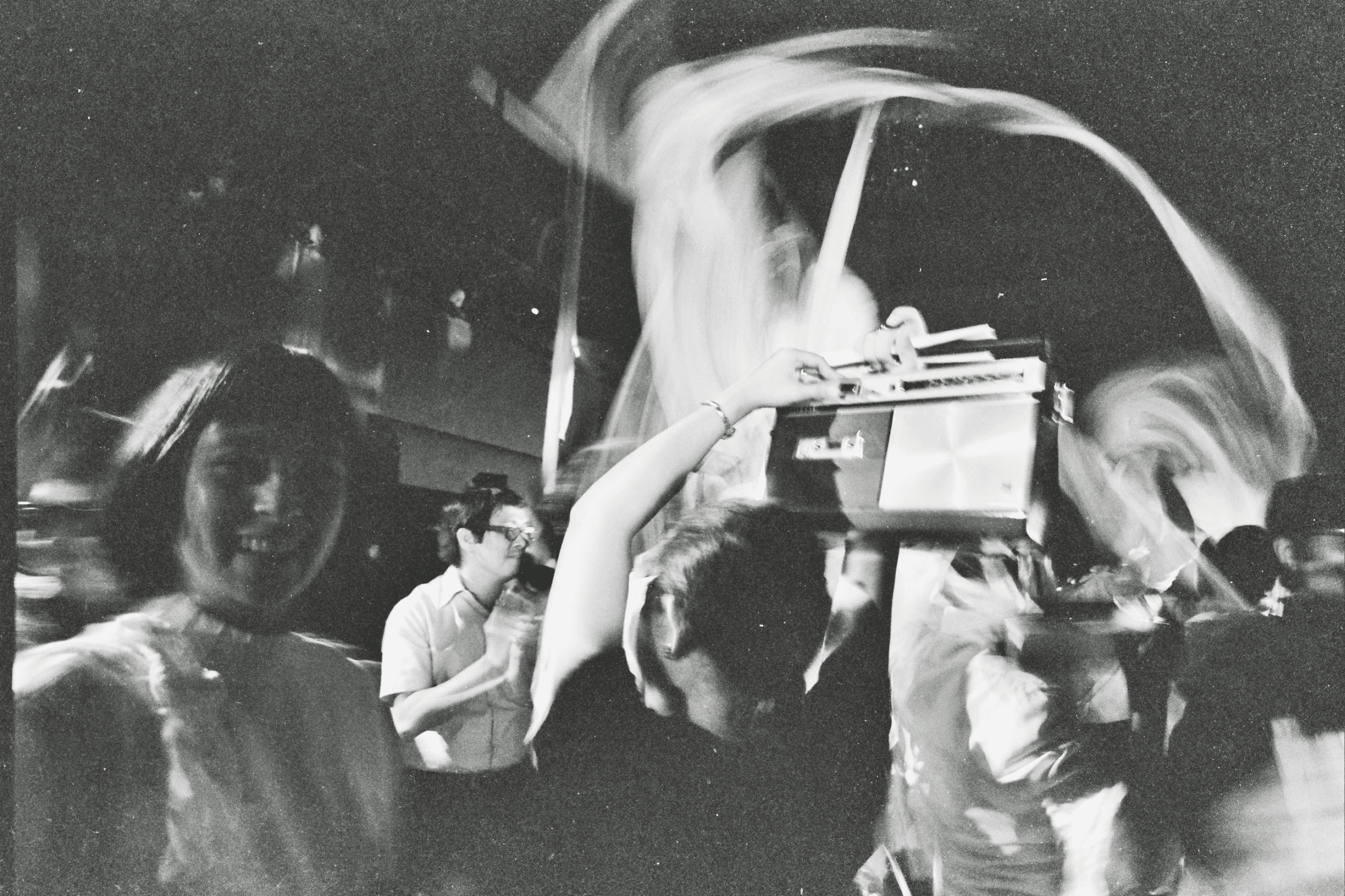 A black-and-white scene of people smiling and dancing energetically, with one person holding a boombox.