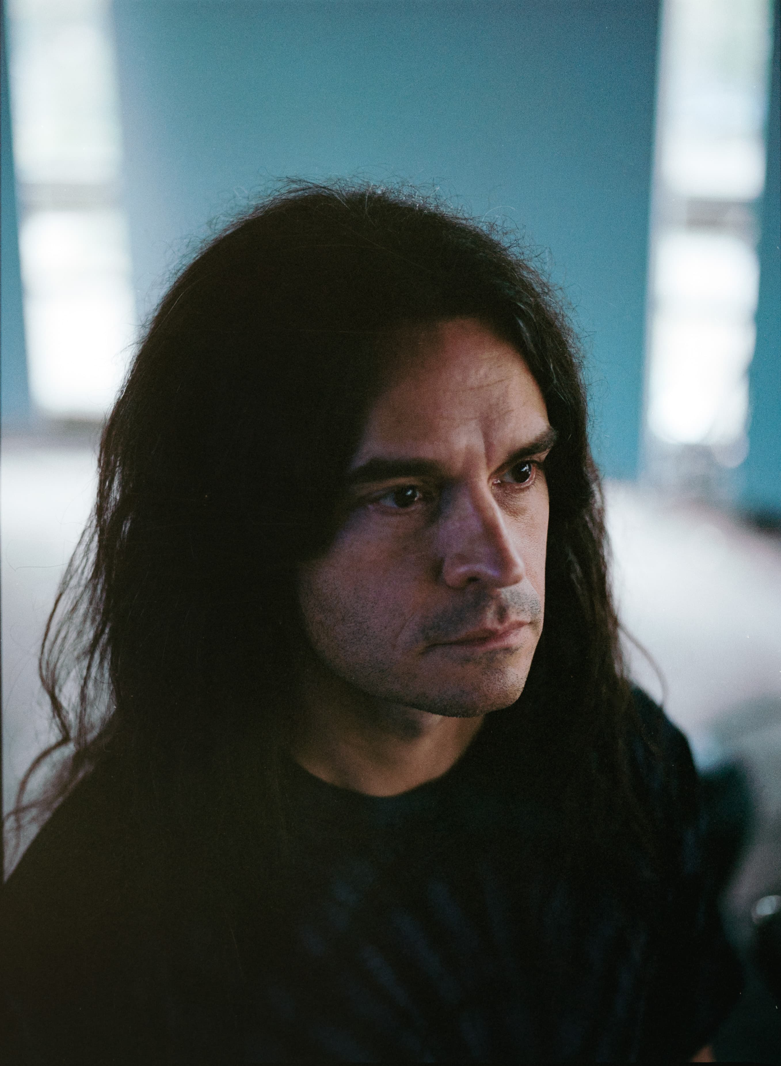 A person with long dark hair is looking to the side in a softly lit room.