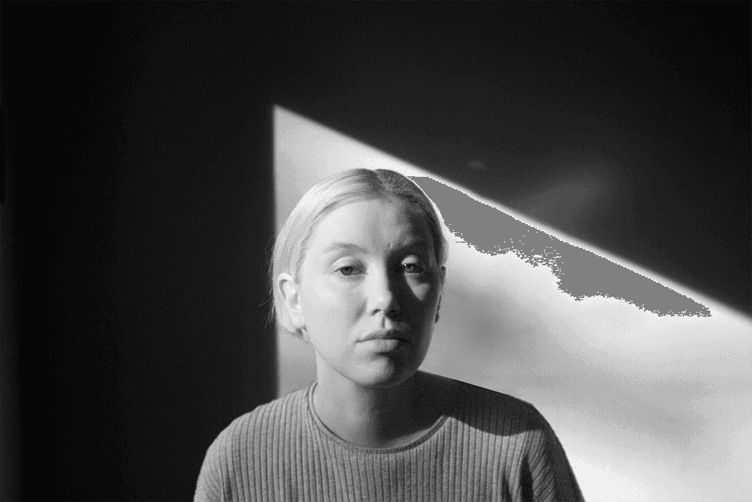 A person with short hair is illuminated by a triangular beam of light against a dark background.