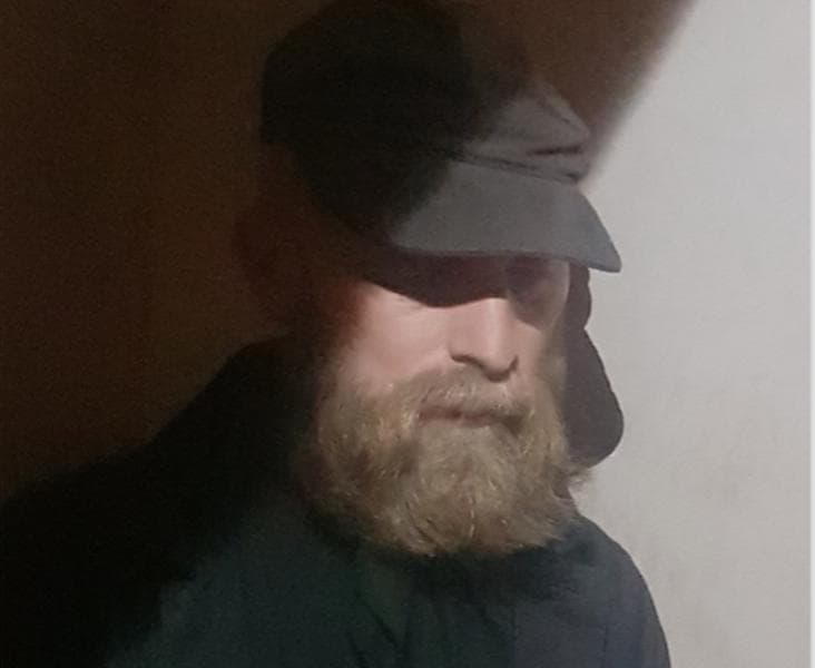 A person with a beard and a cap is partially illuminated by light, creating a shadowed effect on the face.