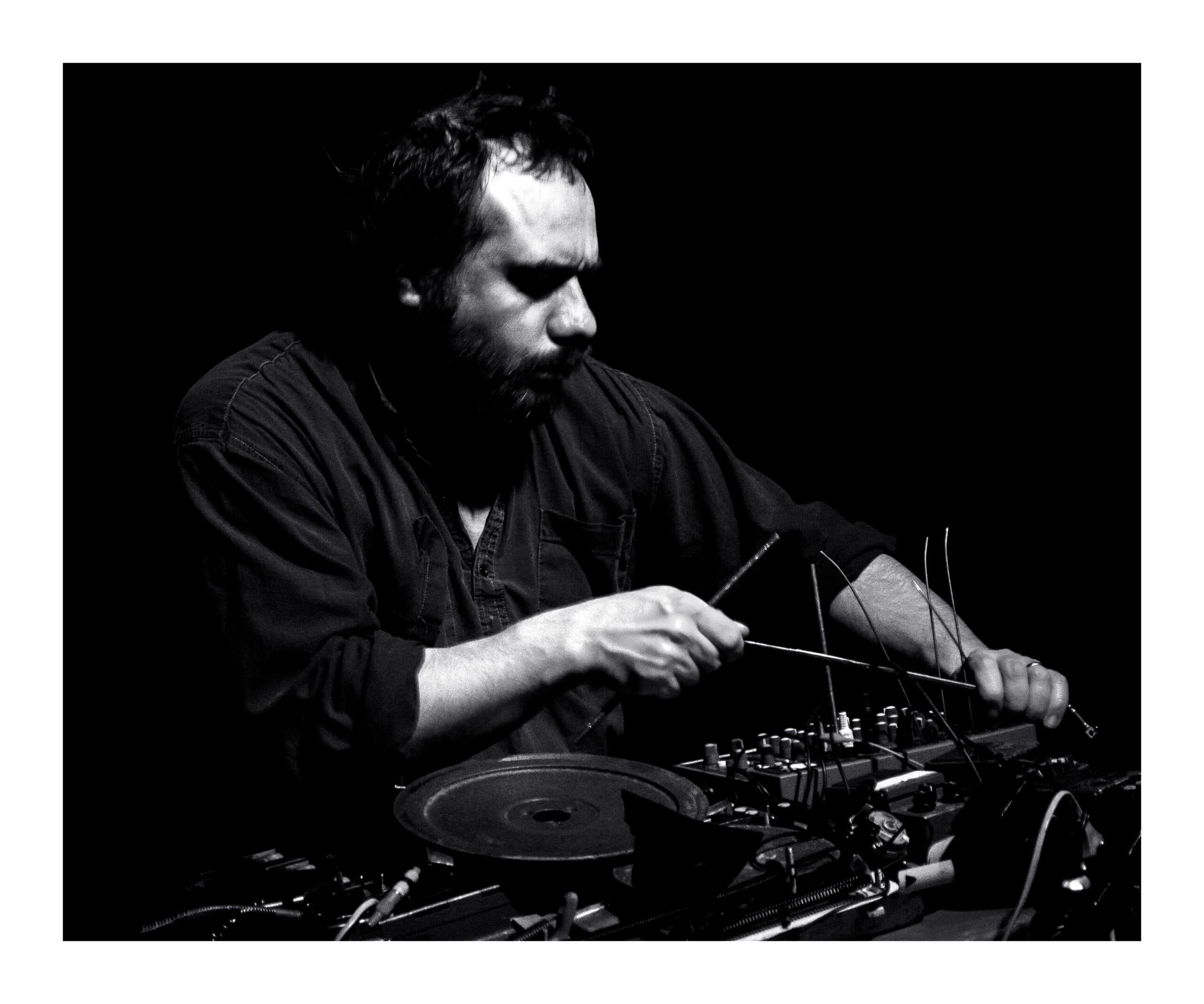 A person is intensely focused on manipulating electronic equipment with metal rods in a dark setting.