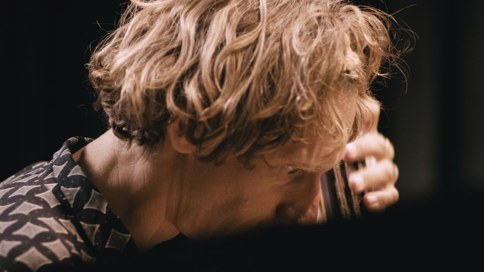A person with wavy blonde hair is a double bass near their face and looking down.